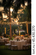 Elegant outdoor wedding reception beautifully decorated with string lights and tables in the evening. Стоковое AI-изображение, AI-художник Юлия Гапеенко / Фотобанк Лори