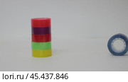 Slow motion of a blue sticky tape rolls across the table next to a pile of red and yellow color sticky tape, with a few rolls slowing moving in front. Стоковое видео, видеограф Дмитрий Нечаев / Фотобанк Лори