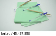 Pens and pencils fall from above on pack of green school notebooks, isolates on white background. Стоковое видео, видеограф Дмитрий Нечаев / Фотобанк Лори