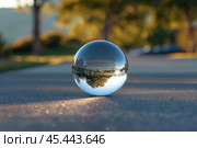 Crystal ball sitting on asphalt reflecting sunset over street. Стоковое AI-изображение, AI-художник Иван Рябоконь / Фотобанк Лори