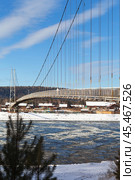 View of the pedestrian cable-stayed bridge connecting the Siberian village of Shamanka on both banks of the Irkut River in November sunny day during ice formation. Rural landscape. Irkutsk region. Russia. Стоковое фото, фотограф Виктория Катьянова / Фотобанк Лори