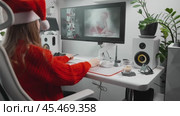 Neural network gradually creates an image on monitor screen. Young female designer in red Santa hat on Christmas Eve watches and evaluates New Year's image created with help of AI and neural network. Стоковое AI-видео, аниматор Енваев Андрей / Фотобанк Лори