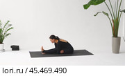 Woman leading healthy lifestyle doing head to knee bend clasping legs with hands, comments on correctness of execution, practicing sitting on mat in room in black sportswear. Стоковое видео, видеограф Сергей Чайко / Фотобанк Лори