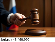A hand with a wooden judge's hammer on the background of the Russian flag. Стоковое AI-изображение, AI-художник RamA / Фотобанк Лори