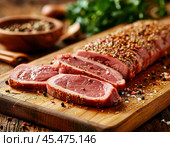 On the kitchen table on a wooden board lie pieces of thinly sliced ​​raw pork tenderloin sprinkled with spices on top. Enjoy your meal! Стоковое AI-изображение, AI-художник Сергей Елизарьев / Фотобанк Лори