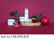 Presentation of natural cosmetics: anti-aging face creams, eyelids and moisturizing gel with extract of pomegranate on wooden podium and burgundy background. Using vitamin fruit extracts for cosmetics. Стоковое фото, фотограф Виктория Катьянова / Фотобанк Лори
