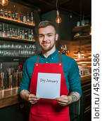 The bartender stands behind the bar and holds a sign with the text "Dry January" in his hands. Sober January, the Month of abstinence from alcohol. Стоковое AI-изображение, AI-художник Ирина Ручушкина / Фотобанк Лори