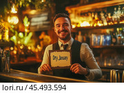 The bartender stands behind the bar and holds a sign with the text "Dry January" in his hands. Sober January, the Month of abstinence from alcohol. Стоковое AI-изображение, AI-художник Ирина Ручушкина / Фотобанк Лори