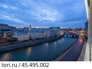 A tranquil city river is highlighted at dusk, reflecting the glowing lights of historic buildings along its banks. A bridge connects both sides, adding charm to the landscape. Стоковое фото, фотограф Алексей Климкин / Фотобанк Лори