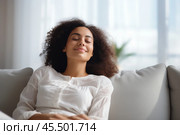 Sweet idleness. Lazy young hispanic lady sit in relaxed pose on big comfy sofa at living room interior breath air dream imagine. Successful female new flat apartment buyer rest at home feel pleasure. Стоковое AI-изображение, AI-художник Sergey Grishin / Фотобанк Лори