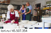 Mature woman learning how to create pottery on potter wheel in a workshop. Стоковое видео, видеограф Яков Филимонов / Фотобанк Лори