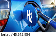 Close-up of a blue hydrogen fuel pump filling a car with 'H2' displayed on the cap in a clean outdoor setting. Стоковое AI-изображение, AI-художник Igor Tichonow / Фотобанк Лори
