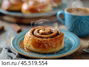 Close-up of a freshly baked cinnamon roll with a steaming hot coffee cup next to it on wooden cafe table. Sweet cinnamon buns American cuisine. Cinnabon with spices and vanilla cream sauce. Breakfast. Стоковое AI-изображение, AI-художник Марина Демидюк / Фотобанк Лори