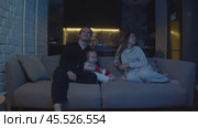 Mom and dad are enjoying their time with their little girl, watching TV and having good time together before going to bed. Стоковое видео, видеограф Strunov David / Фотобанк Лори