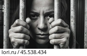 A woman peers through prison bars with a forlorn expression. The stark black-and-white photograph captures the despair of confinement, with her gaze seeking beyond the bars. Стоковое AI-видео, аниматор Ольга Сухарева / Фотобанк Лори