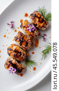 Вкусные куриные рулетики на гриле со съедобными цветами и травами на белом фоне для свежего кулинарного наслаждения. Стоковое AI-изображение, AI-художник ФотоИнтеллект / Фотобанк Лори