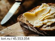 Slice of wholemeal bread with butter curl. Buttering toast. Yellow butter scattered on a piece of bread. Bread with toasting and spreading butter. Generous spread of butter on a rustic bread slice. Стоковое AI-изображение, AI-художник Марина Демидюк / Фотобанк Лори