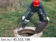 Worker opens septic well manhole cover. septic tank maintenance and sewage pumping. Стоковое фото, фотограф Коханова Наталья / Фотобанк Лори