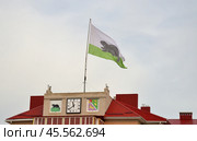 Bobrov, Voronezh region, Russia, October 17, 2022:  Clock on tower of residential building under flag and next to Bobrov coat of arms in center of square with fountain. Редакционное фото, фотограф Алексей Антипов / Фотобанк Лори