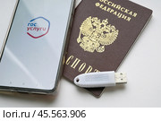 Устройство  USB eToken  (рутокен) белого цвета, устройство для хранения электронной цифровой подписи (ЭЦП) и информации для аутентификации пользователя, паспорт и телефон с приложением Госуслуги на белом фоне. Редакционное фото, фотограф Snezka / Фотобанк Лори