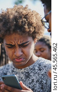 Young man frowning while using phone with friends watching him. Стоковое AI-видео, аниматор Юрий Поздников / Фотобанк Лори