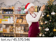 Guy employee decorates trading floor of minimarket by tinsel at New Year Eve. Стоковое фото, фотограф Яков Филимонов / Фотобанк Лори