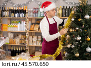 Guy employee decorates trading floor of minimarket by tinsel at New Year Eve. Стоковое фото, фотограф Яков Филимонов / Фотобанк Лори