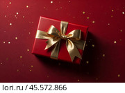 Perfect red Christmas present gift box with elegant gold bow ribbon on red background near stars. Greeting gift symbolize lovely holiday gifting. Birthday Christmas festive concept. Copy ad text space. Стоковое AI-изображение, AI-художник Aleksandr Golubev / Фотобанк Лори