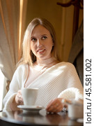 Beautiful young woman is drinking coffee. Attractive woman in a cozy cafe. Pretty woman in a white sweater with a cup of cappuccino in her hands. Стоковое фото, фотограф Андрей Степанов / Фотобанк Лори