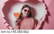Charming moment: beautiful young woman with heart in her hands on pink background in heart frame sends video card to her beloved. Bright embodiment of tenderness and celebration valentines day. Стоковое видео, видеограф Енваев Андрей / Фотобанк Лори