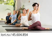 Young concentration girl maintaining mental and physical health attending group yoga class at studio, practicing twisting poses. Стоковое фото, фотограф Яков Филимонов / Фотобанк Лори