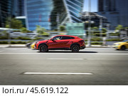 Lamborghini Urus moving on the street in Moscow. Red SUV supercar is driving in front of office buildings. Редакционное фото, фотограф Константин Григорьев / Фотобанк Лори
