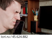 Парень крепко зажмурил глаза, прикрыл рот смартфоном. Стоковое фото, фотограф Vladislav_v / Фотобанк Лори