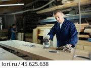 During manufacturing, man employee grinds surface of wooden board, gives smoothness to surface. Стоковое фото, фотограф Яков Филимонов / Фотобанк Лори