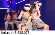 Cheerful young female friends wearing VR headsets and holding controllers having fun in virtual reality studio, competing in two-on-two shooter game. Стоковое видео, видеограф Яков Филимонов / Фотобанк Лори