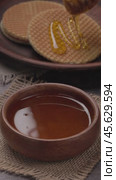 Drops of honey slowly flowing from a wooden honey dipper into a honey bowl, close-up. Honey flowing from a wooden honey dipper on to holland waffles. Vertical video. Стоковое видео, видеограф Андрис Салминьш / Фотобанк Лори