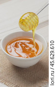 Drops of honey slowly flowing from a wooden honey dipper into a honey bowl, close-up. Honey flowing from a wooden honey dipper on to holland waffles. Vertical video. Стоковое видео, видеограф Андрис Салминьш / Фотобанк Лори