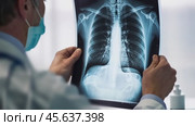 View from the back of a serious doctor examining the results of an MRI. A male specialist working in a hospital examines a patient's chest x-ray. Medicine and hospital concept. Medical health care. Стоковое AI-видео, аниматор Евгений Демидюк / Фотобанк Лори
