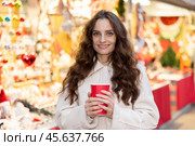 Smiling woman walking through Christmas street market with warm beverage in paper cup. Стоковое фото, фотограф Яков Филимонов / Фотобанк Лори