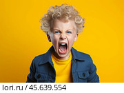 A child with curly blonde hair is expressing intense emotions, likely frustration or excitement, in front of a bright yellow backdrop. His energy is palpable. Стоковое AI-изображение, AI-художник Sergey Grishin / Фотобанк Лори