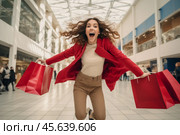 A woman with curly hair expresses pure joy as she jumps in a shopping mall, clutching red bags. The bright atmosphere highlights her exhilaration and the hustle of the shopping crowd. Стоковое AI-изображение, AI-художник Sergey Grishin / Фотобанк Лори