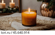 A mock-up of a cozy burning candle made of amber glass with an empty white label in a festive, New Year's home interior. Стоковое AI-изображение, AI-художник Photojuli / Фотобанк Лори