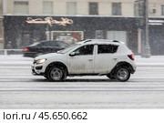 Side view rolling shot with Renault Sandero Stepway subcompact car. Fast moving white small hatchback in snowfall with motion blur effect. Редакционное фото, фотограф Константин Григорьев / Фотобанк Лори