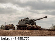 Тяжёлая военная техника армии России: САУ МСТА-С и БТР-82А стоят рядом с укрытием. Вооруженные силы РФ: гаубица 2с19м2 и бронетранспортёр под серыми облаками. (2019 год). Редакционное фото, фотограф Евгений Зимин / Фотобанк Лори