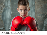 A boy in boxing gloves strikes, a cute teenage boy stands in a fighter's pose, ready to fight. Playing sports. Children's sports sections. Стоковое AI-изображение, AI-художник Photojuli / Фотобанк Лори