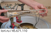 A male master demonstrates a burnt-out boiler heating element covered with lime coating, rotating it. Electric Water Heater Maintenance and Repair. Стоковое видео, видеограф Мария Зубарева / Фотобанк Лори