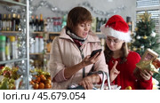 Family with basket shopping at supermarket, looking for something to buy and checking with mobile phone. Christmas shopping. Стоковое видео, видеограф Яков Филимонов / Фотобанк Лори