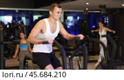Guy performs exercises with stationary air bicycle in gym. Стоковое видео, видеограф Яков Филимонов / Фотобанк Лори