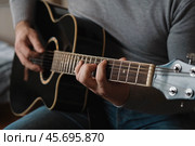 Playing the guitar. Strumming acoustic guitar. Musician plays music. Man fingers holding mediator. Man hand playing guitar neck in dark room. Unrecognizable person rehearsing, fretboard close-up. Стоковое фото, фотограф Марина Демидюк / Фотобанк Лори