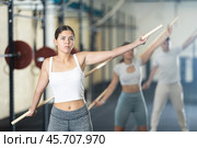 Slender girl, together with other athletes, does a warm-up using a long stick in gym. Стоковое фото, фотограф Яков Филимонов / Фотобанк Лори